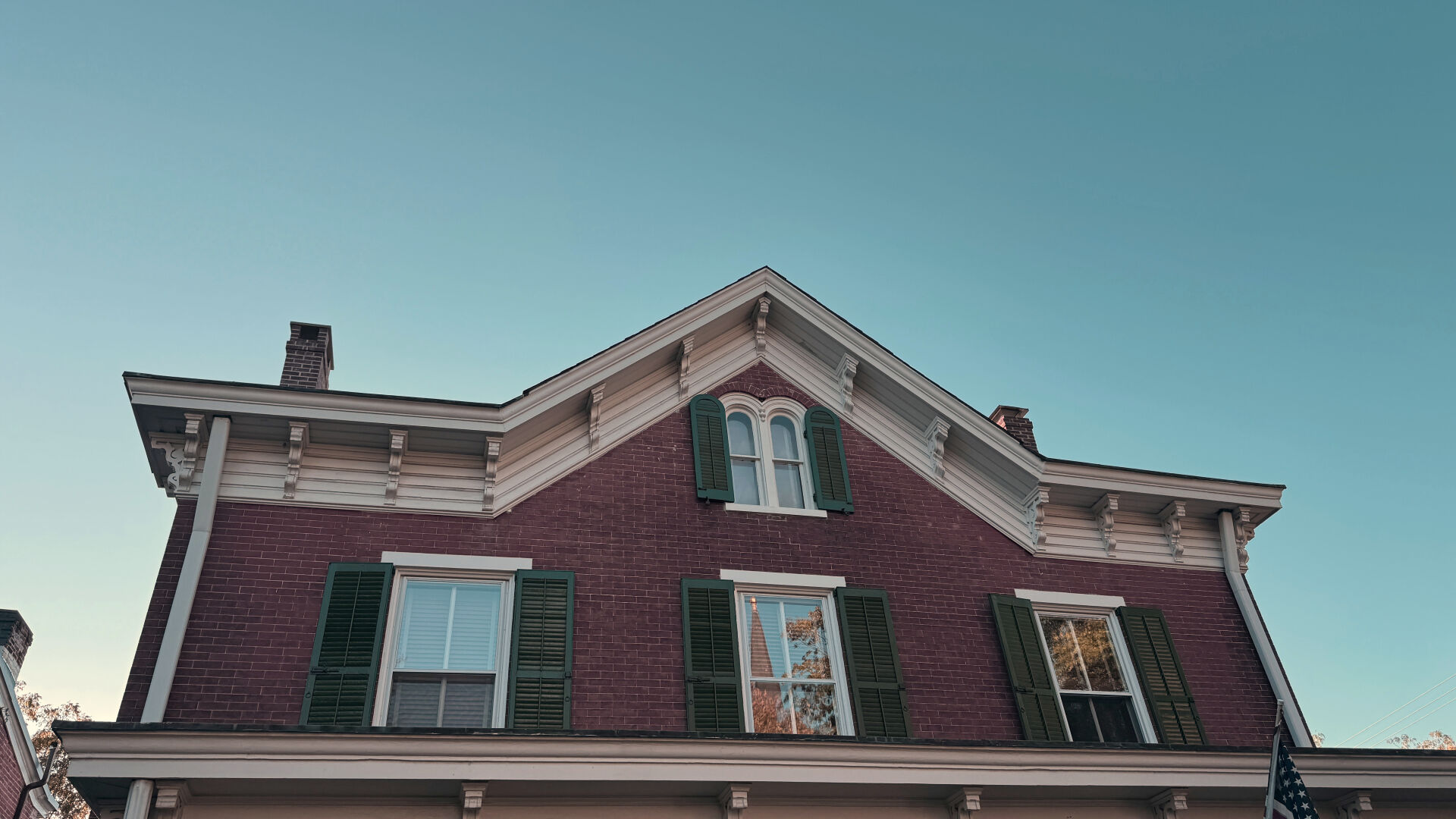 The gabled roof of a 19th century house. Brick with white trim.

Blue sky