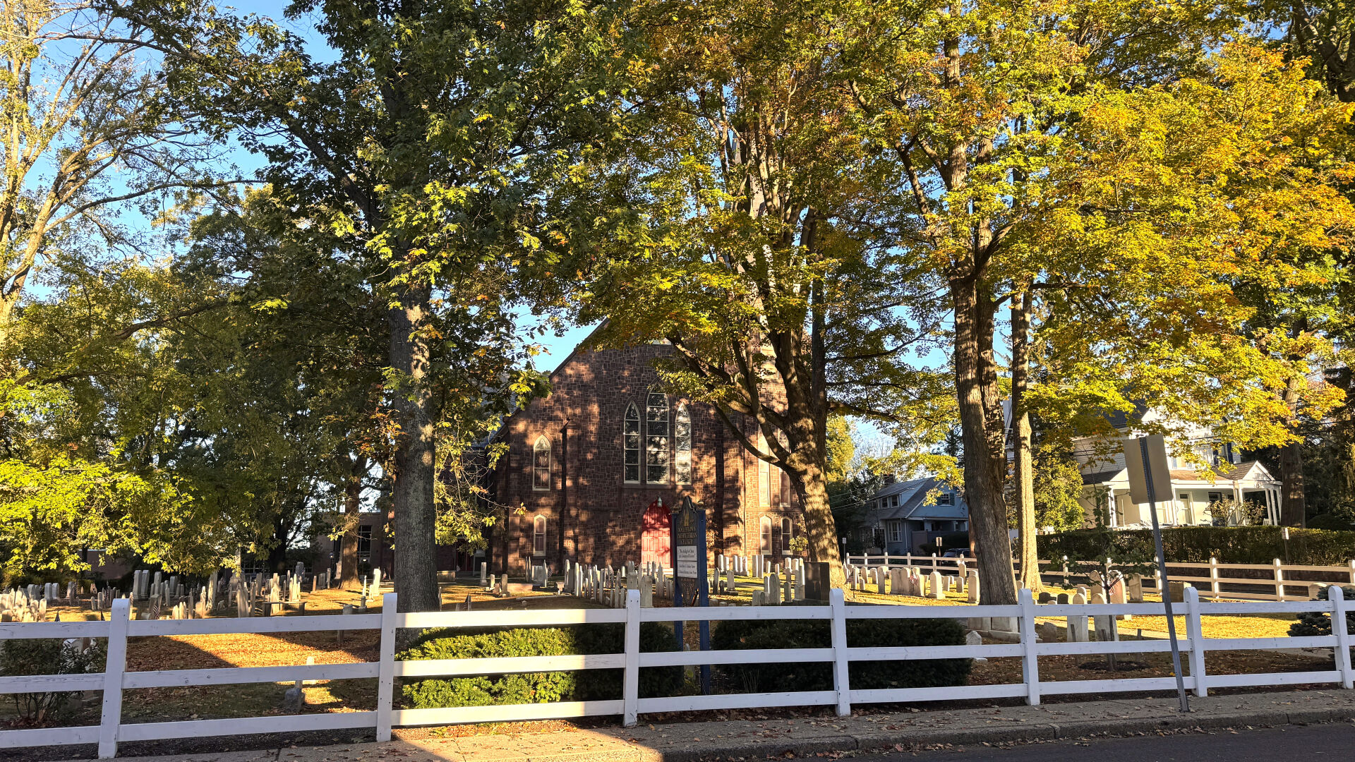 The Presbyterian Church in Doylestown peaking out from behind fall foliage and the grave yard is in front of it.